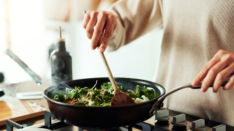 Person cooking food in frying pan on stovetop.