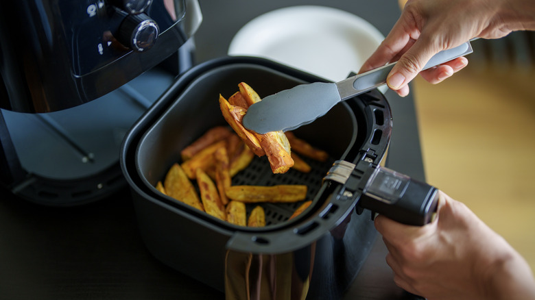 Person removing fries from an air fryer using a pair of stainless steel tongs.