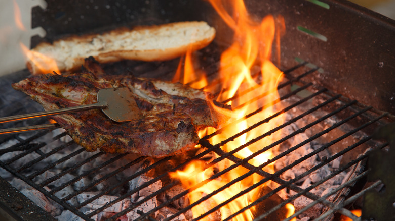 Tongs holding a steak over a flaming outdoor grill.