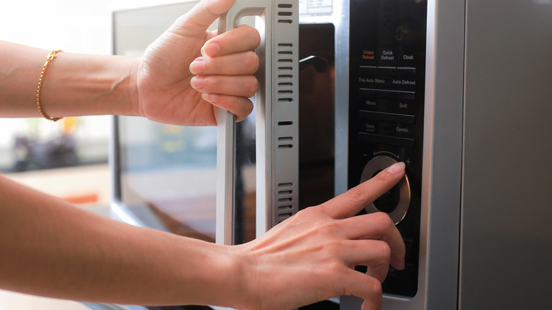 Hands opening a silver microwave