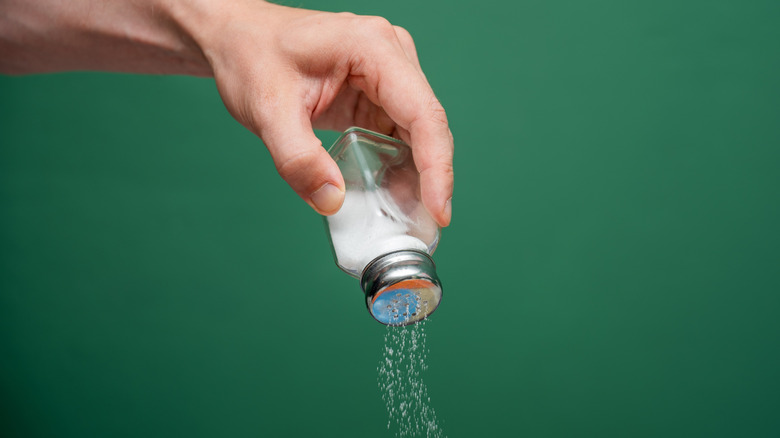 A hand sprinkles salt out of a shaker