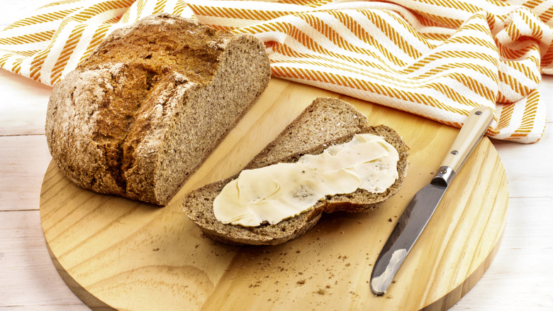 Cut loaf of soda bread with slice smeared with butter next to knife
