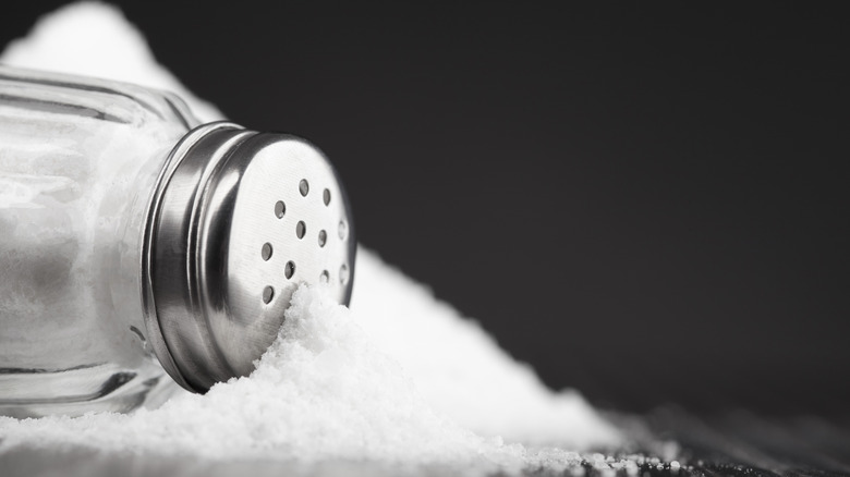 Salt shaker spilling salt on black background