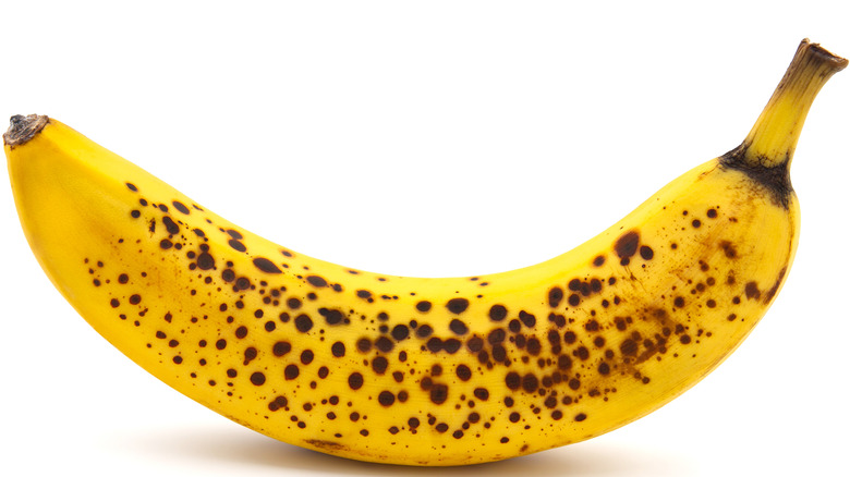 A yellow banana with lots of brown spots on a white back ground