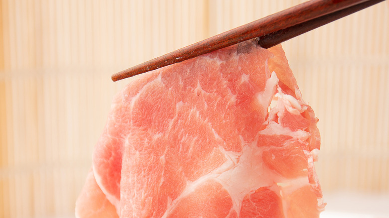 A pair of chopsticks lifting up a piece of raw pork