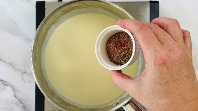 hand holding seasonings above a metal pot full of liquid