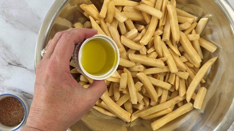 hand holding a cup of oil over a bowl of fries