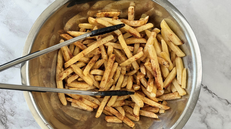 metal tongs in a bowl of seasoned fries