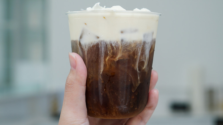 Hand holding foamy iced coffee