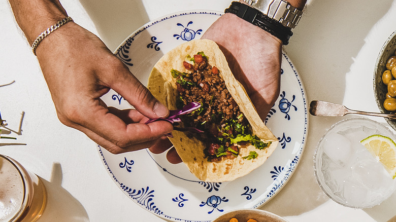 hands putting toppings on taco