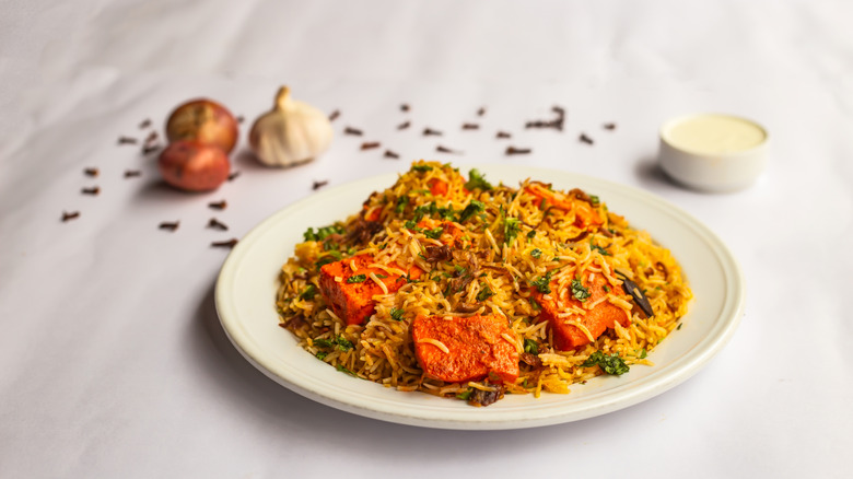 Paneer rice on a white plate with onions and a sauce on the side