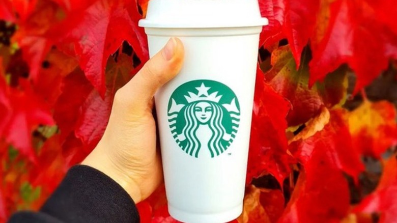 person holding cup of Starbucks coffee in front of changing fall leaves