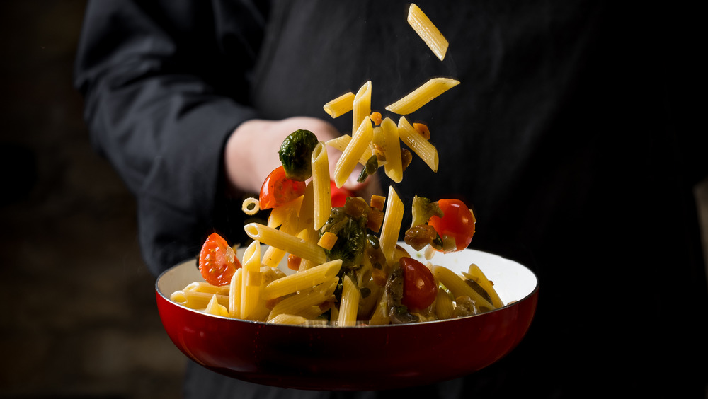 Person tossing pasta with black clothes