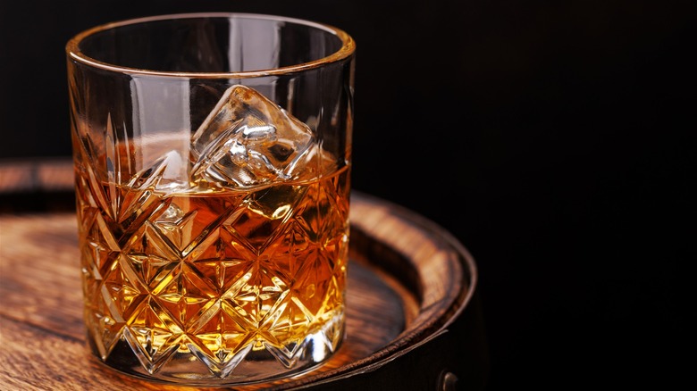 Close-up shot of a glass of Scotch whisky on the rocks, set on top of a wooden barrel.