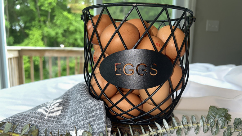 Black metal basket with brown eggs, towel, and greenery