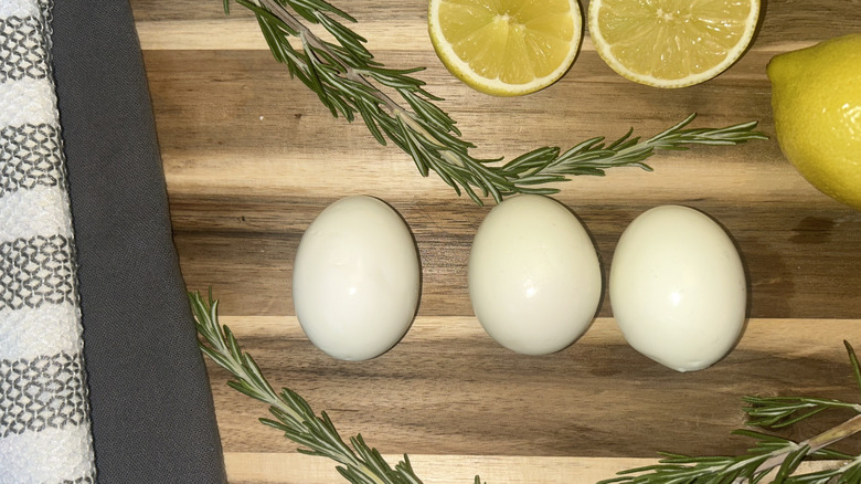 Eggs on cutting board with two gray towels, rosemary, and lemon
