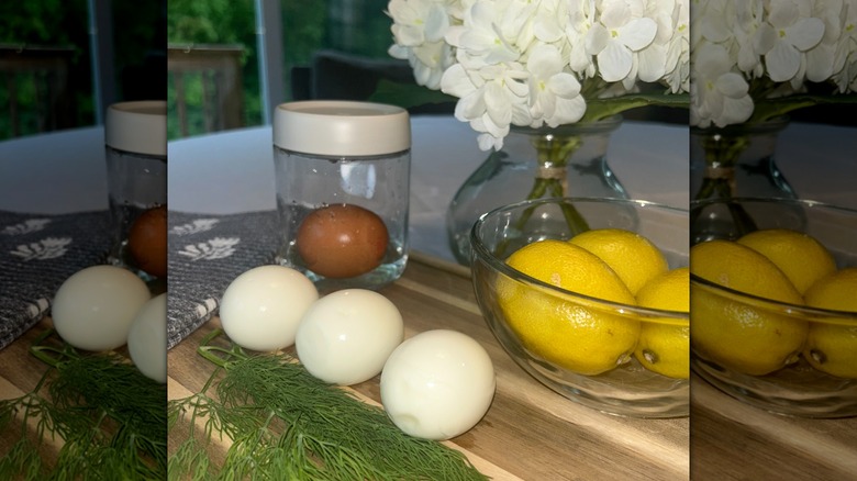 Three eggs on cutting board with bowl of lemons, dill, and jar with egg