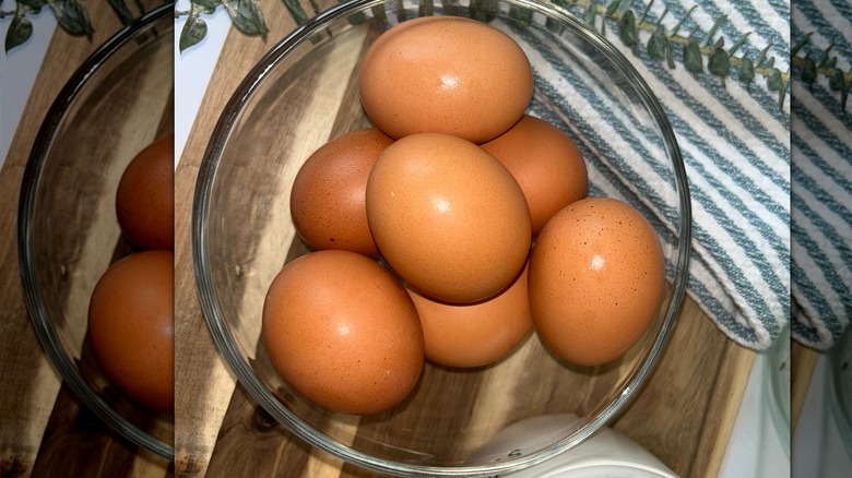 Eggs in a glass bowl with greenery and tea towel on a wooden board