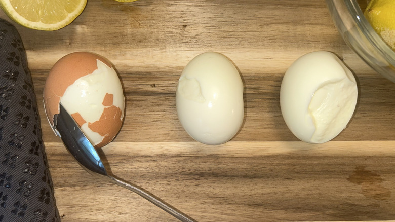 Three eggs on wooden cutting board with spoon, lemons, and gray oven mitt