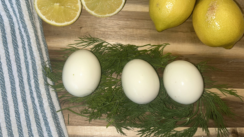 Three eggs nestled on dill with lemons and green and white striped towel