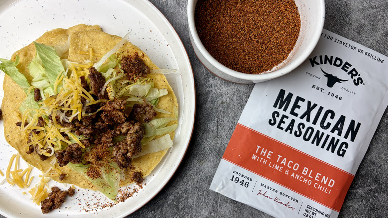 Kinder's The Taco Blend with Lime & Ancho Chili Mexican Seasoning packet, seasoning in a white ramekin, and taco on a white plate