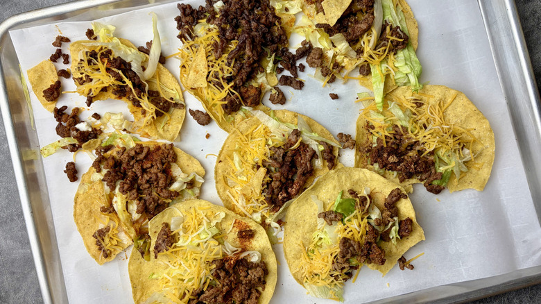 8 prepared tostadas with taco meat for tasting side-by-side on a baking sheet lined with parchment paper