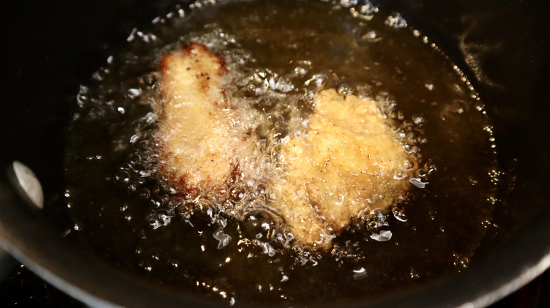 two chicken tenders in a pot with bubbling oil