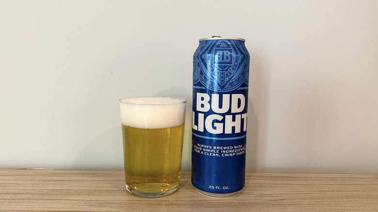 A glass of Bud Light with a thick foamy head beside a tall blue Bud Light can