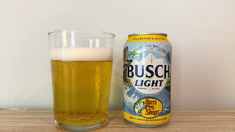 A glass of Busch Light beside a Busch Light can, with a fizzy golden beer and a foamy head
