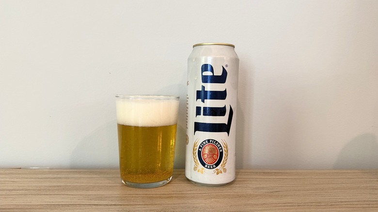 A glass of Miller Lite next to a tall white Miller Lite can, with a pale golden beer and a thick head