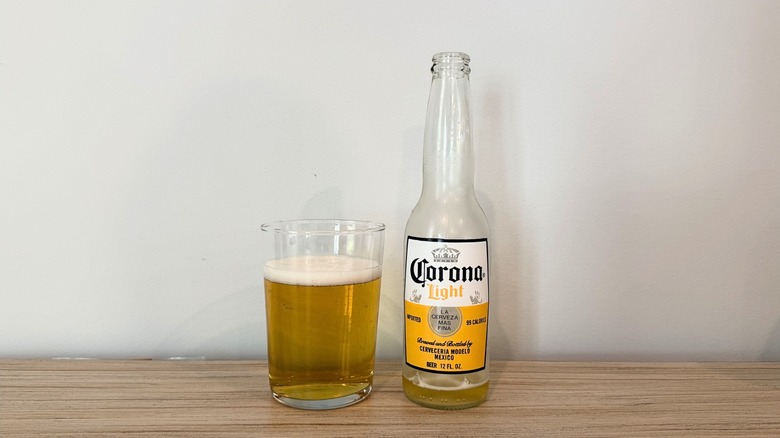 A glass of Corona Light next to a clear Corona Light bottle, with a light golden beer and a thin layer of foam