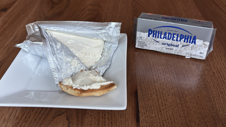 Bite of a bagel with cream cheese on top and a brick of cream cheese next to it