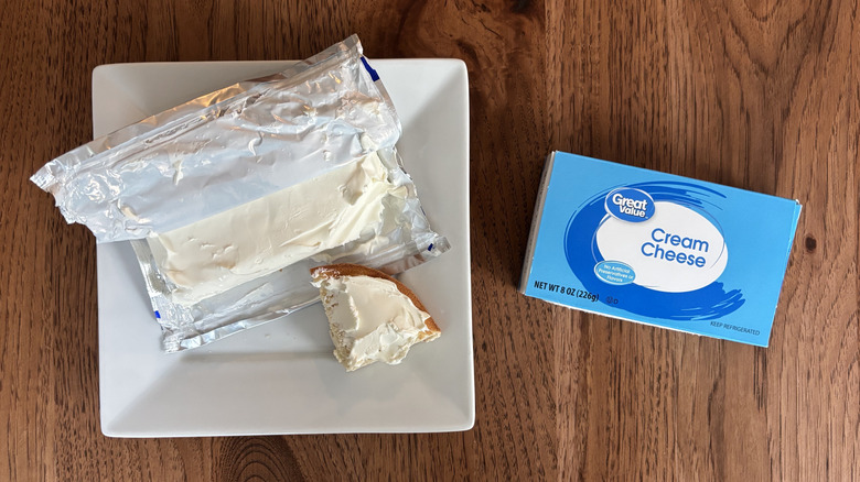 Bagel with cream cheese spread on top, along with block of cream cheese and brand box
