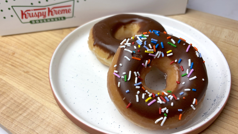 Two Krispy Kreme Chocolate Iced Doughnuts on a plate, with and without sprinkles
