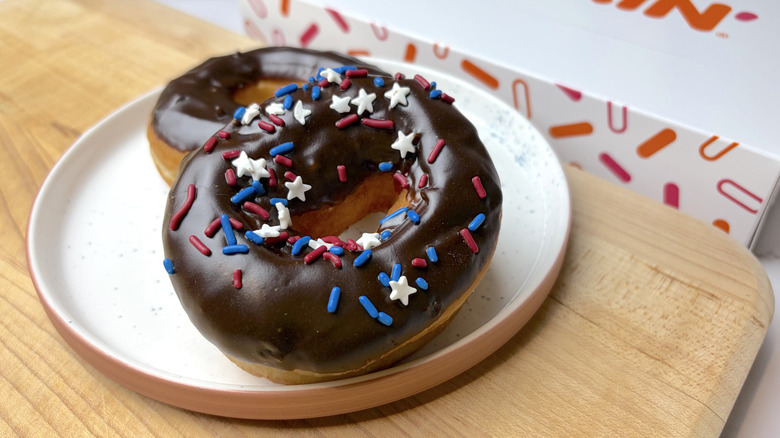 Two Dunkin' Chocolate Frosted donuts on a plate, with and without sprinkles