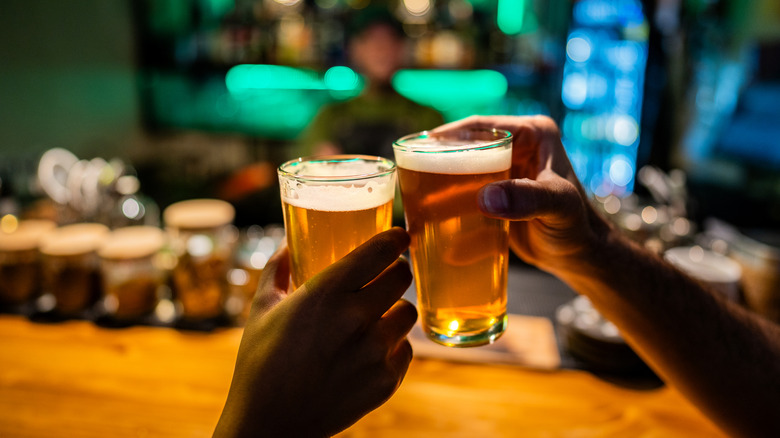 Two people tapping pints of beer together in bar