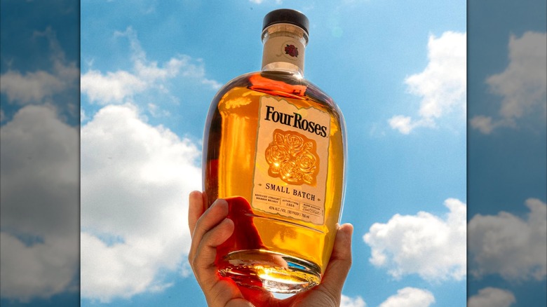 Hand holding Four Roses Small Batch bottle in from of blue sky and clouds