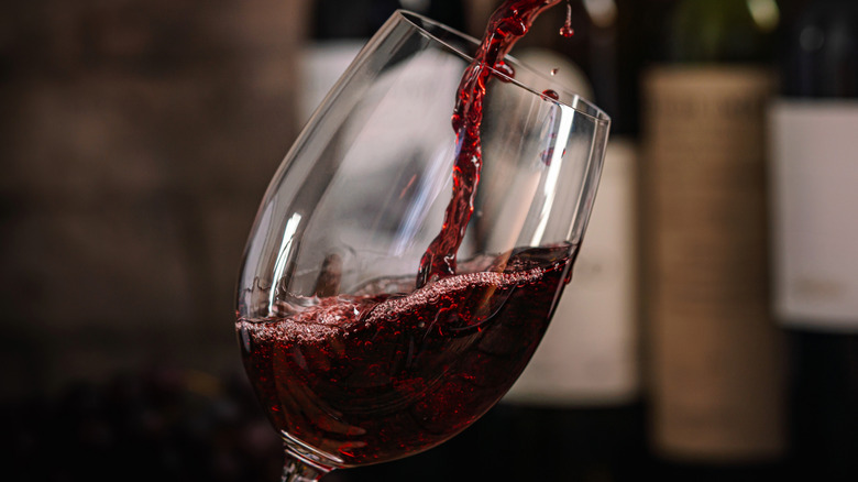 A bottle of red wine being poured into a glass.