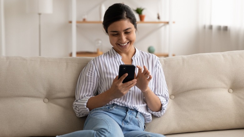 Woman in striped shirt sitting on couch and scrolling through phone
