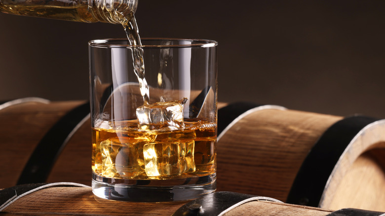 Whiskey pouring into glass on top of barrel.