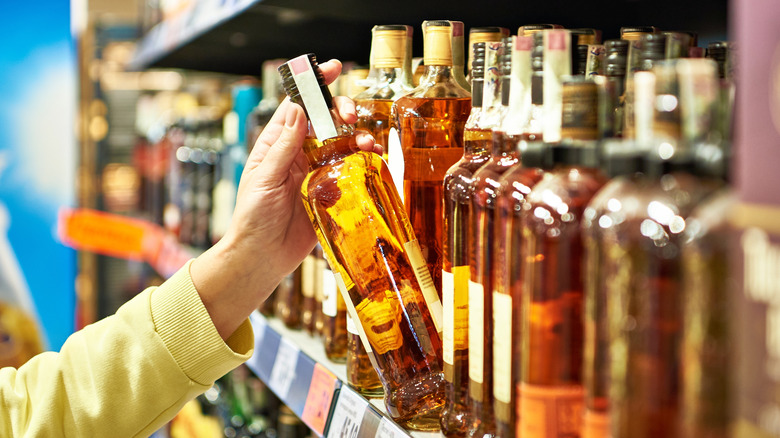 Hand grabbing bottle of liquor off store shelf.
