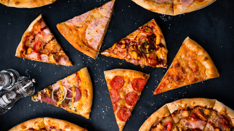 Various meaty pizza slices on a black surface.