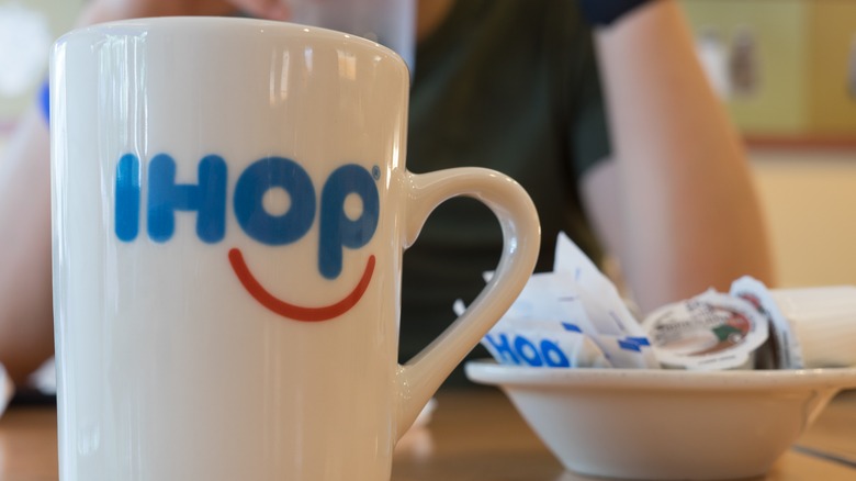 Coffee cup with IHOP logo next to dish of sugar and cream