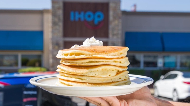 Person holding a stack of pancakes in front of an IHOP restaurant