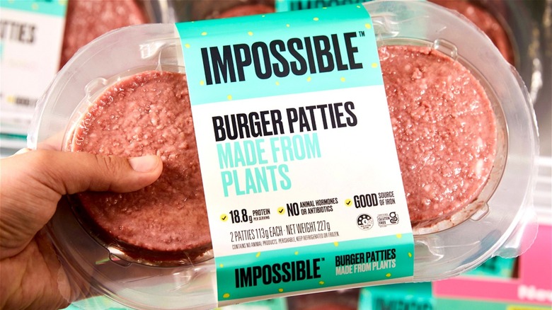 A hand holding a package of Impossible Foods burger patties