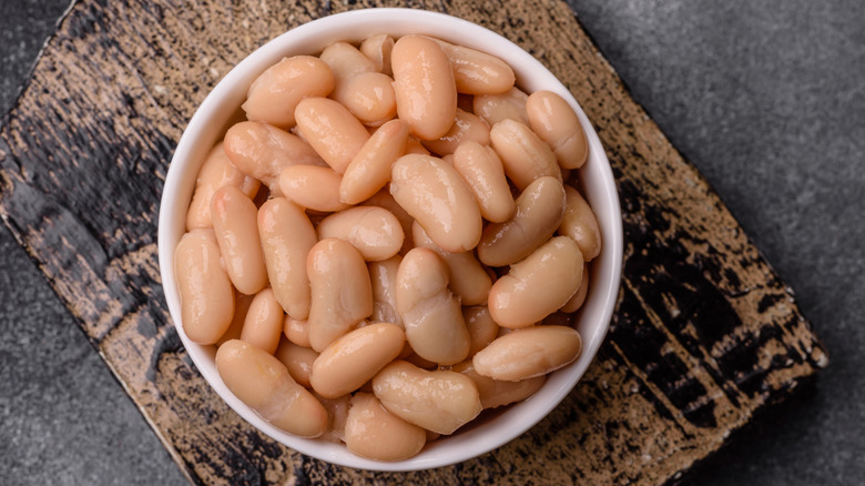 Canned pinto beans poured into a small white bowl on top of a rustic wooden cutting board