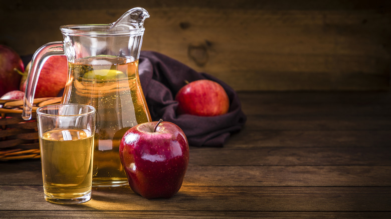 pitcher of apple juice next to a red apple and a glass of juice
