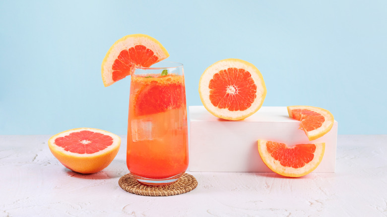 glass of grapefruit juice on a coaster surrounded by slices of fresh grapefruit