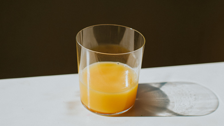 glass that is less than half full of orange juice near the edge of a table