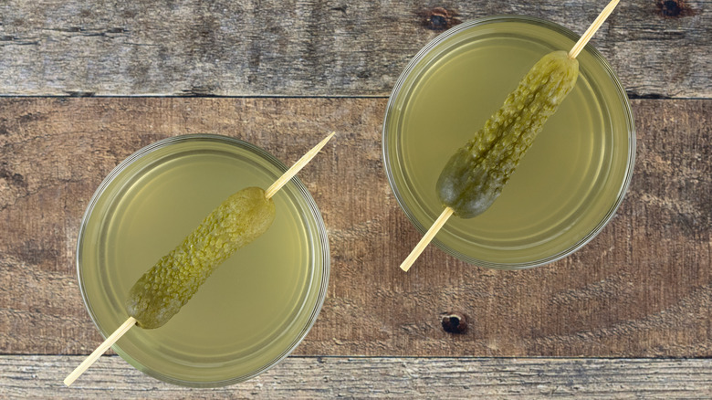 glasses of pickle juice with pickles on skewers resting atop the glasses